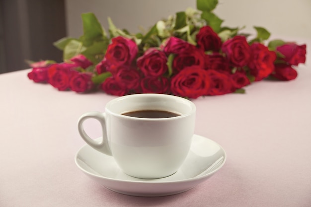 Una taza de café y rosas rojas sobre la mesa.