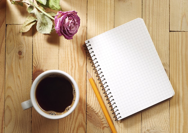 Taza de café, rosas secas y cuaderno sobre una mesa de madera