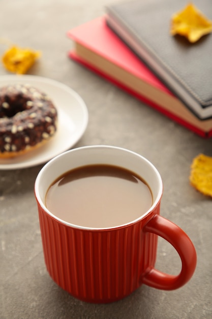 Taza de café, rosquilla y hojas de otoño sobre fondo gris. Concepto de otoño. Foto vertical