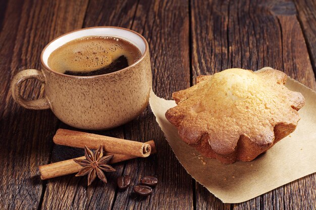 Taza de café y sabroso cupcake en mesa de madera oscura.