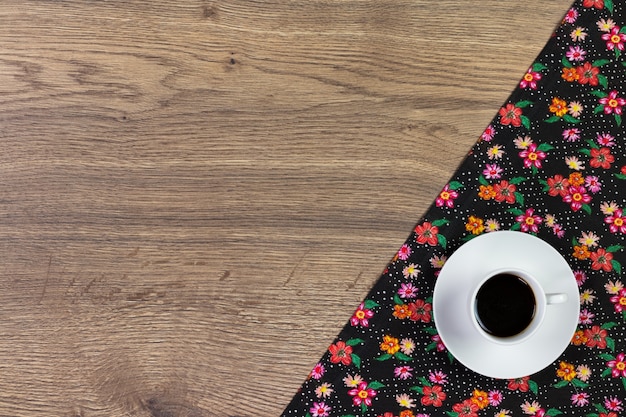 Taza de café y servilleta de tela floral sobre fondo de madera.