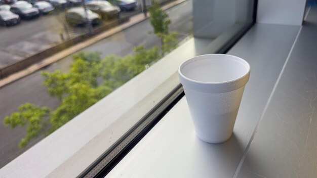 Una taza de café se sienta en el alféizar de una ventana junto a una ventana con vista a la calle.