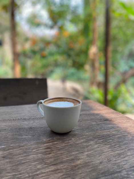 Una taza de café se sienta en una mesa afuera frente a un jardín