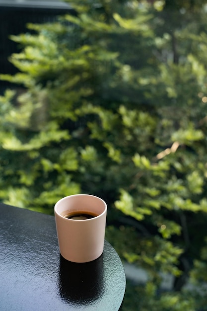 Una taza de café se sienta en una mesa frente a una ventana con un árbol al fondo.