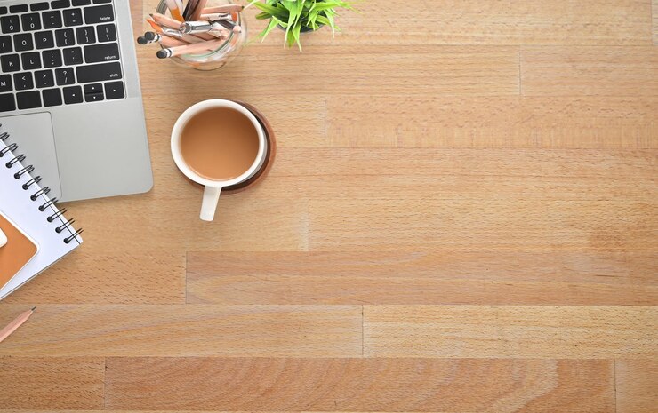 una taza de café se sienta en una mesa de madera junto a una computadora portátil