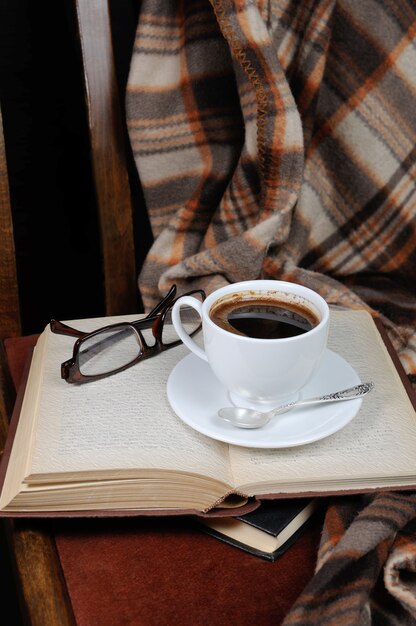 Una taza de café en una silla con una pila de libros y una manta