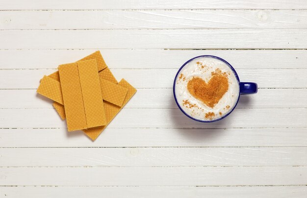 Taza de café con símbolo de forma de corazón y gofres en blanco de madera