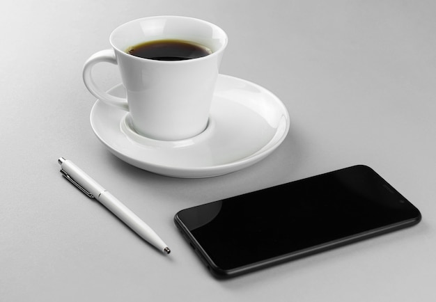 Taza de café smartphone y bolígrafo blanco sobre un fondo gris