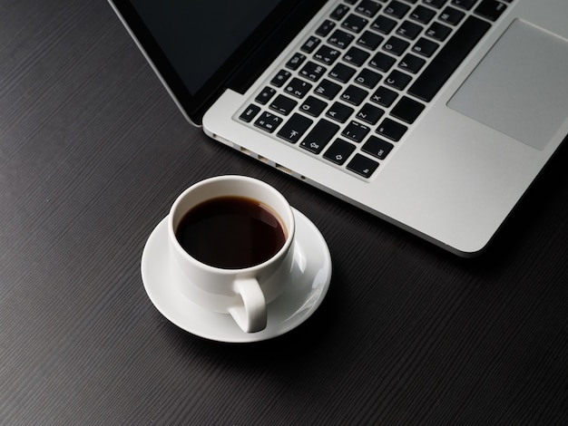 Taza de café sobre la mesa y la computadora portátil.