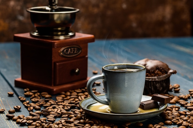 Taza de café sobre una mesa de madera azul con granos de café y chocolate