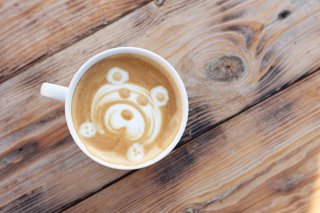 Taza de café sobre una mesa de madera. Capuchino con un patrón de oso. Vista superior