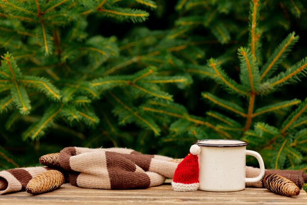 Taza de café y sombrero de Navidad en mesa de madera con ramas de abeto en el fondo