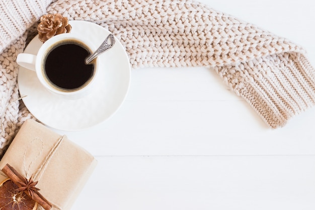 Una taza de café, suéter, caja de regalo artesanal sobre un fondo blanco de madera