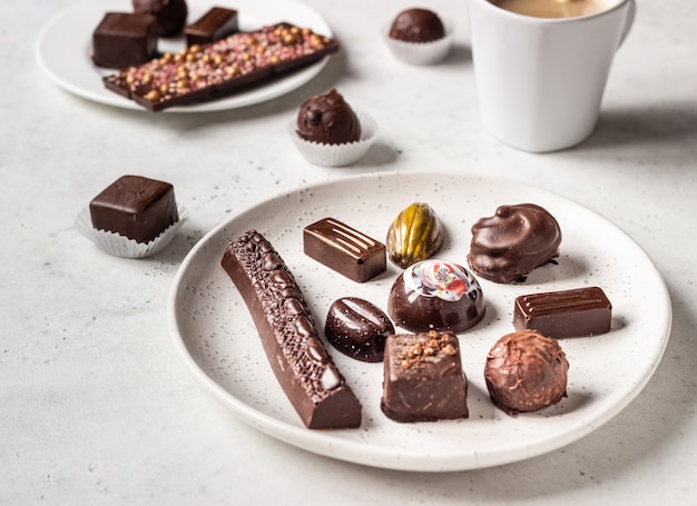 Taza de café y surtido de dulces de chocolate fino sobre fondo de piedra gris.