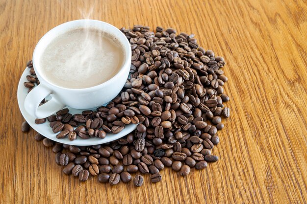 Taza de café en una taza blanca y granos de café en la mesa de madera.