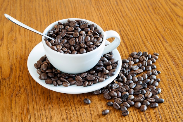 Taza de café en una taza blanca y granos de café sobre fondo de mesa de madera