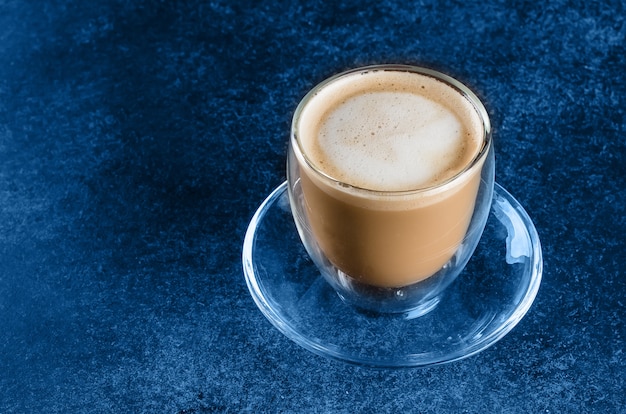 Una taza de café en la taza de cristal en la tabla azul de fondo oscuro. Copia espacio Por la mañana bebida capuchino