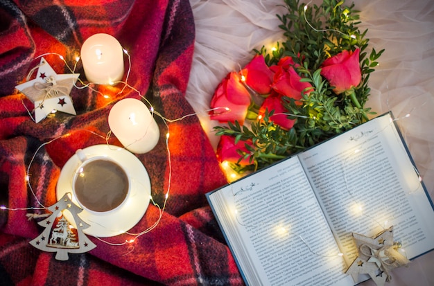 una taza de café (té), rosas rojas con boj, un libro, velas, guirnaldas
