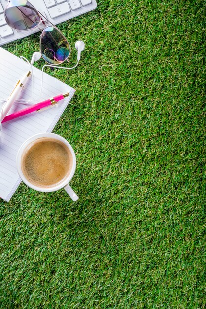 Taza de café, teclado, cuaderno sobre hierba verde