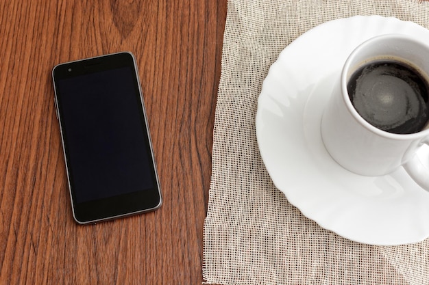 Taza de café y teléfono celular en la mesa de madera