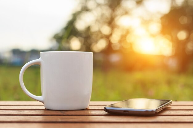 Taza de café y teléfono inteligente en la mesa en el atardecer