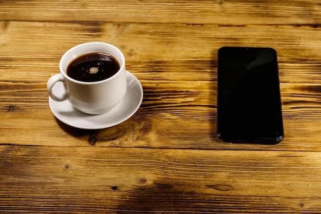 Taza de café y teléfono inteligente en una mesa de madera