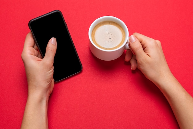 Una taza de café y un teléfono inteligente moderno. pantalla en negro. superficie roja