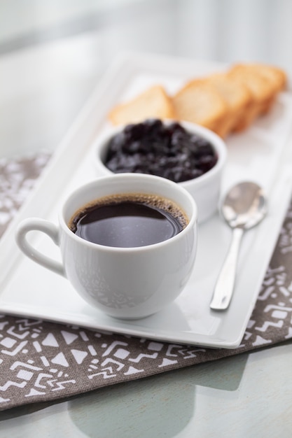 Una taza de café y tostadas con mermelada de arándanos en blanco