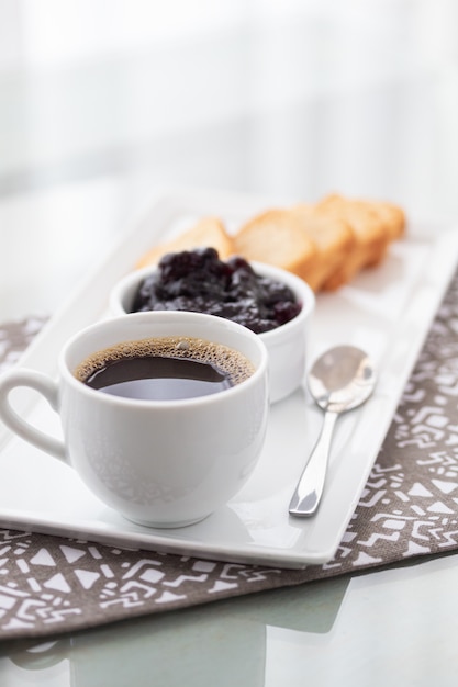 Una taza de café y tostadas con mermelada de arándanos en blanco.