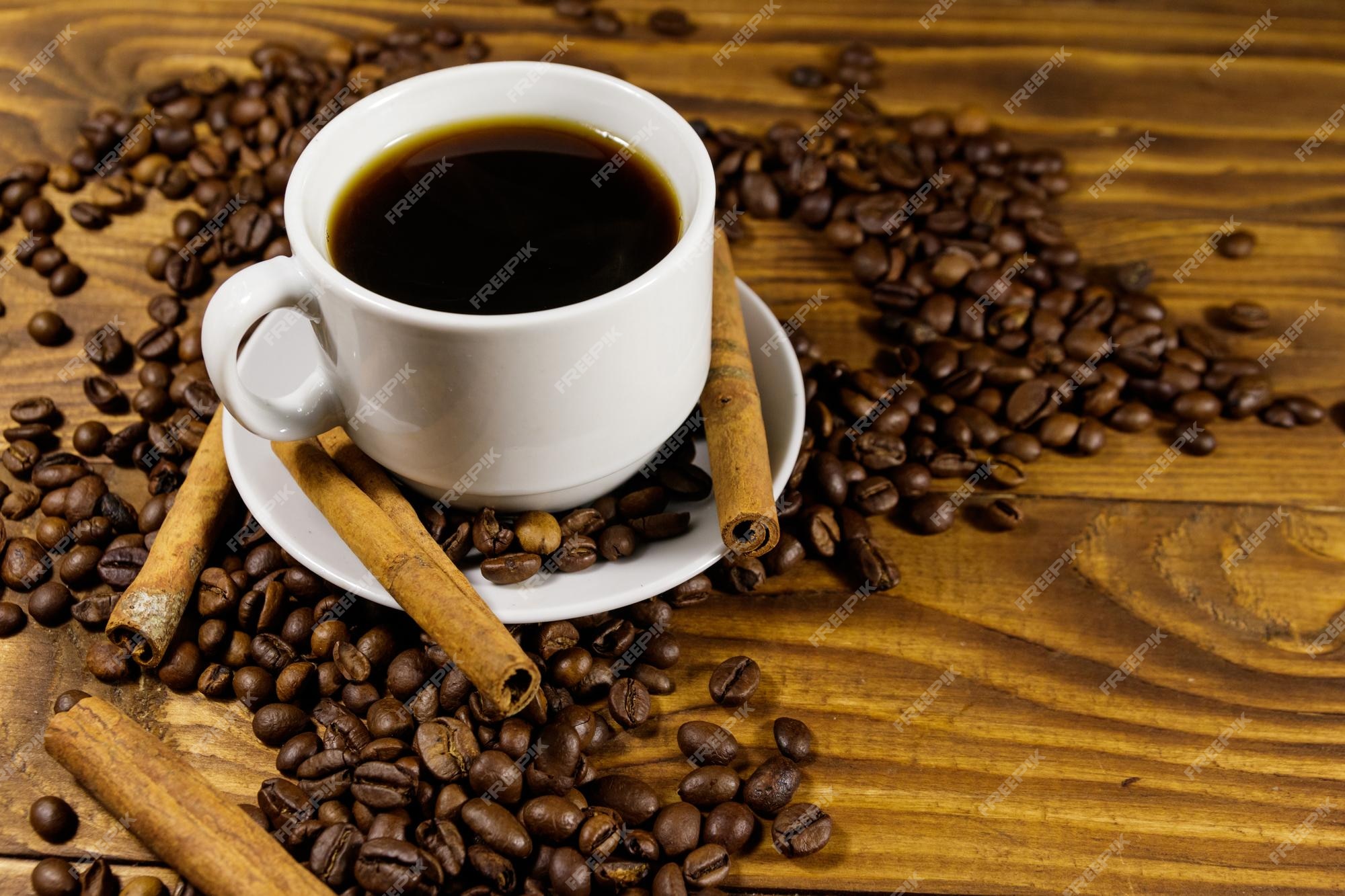 Taza de café tostado en grano y palitos de canela en la mesa de madera