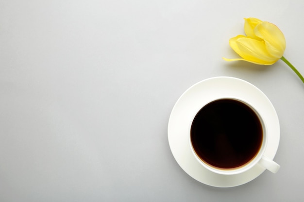 Taza de café con tulipán amarillo sobre superficie gris con espacio de copia