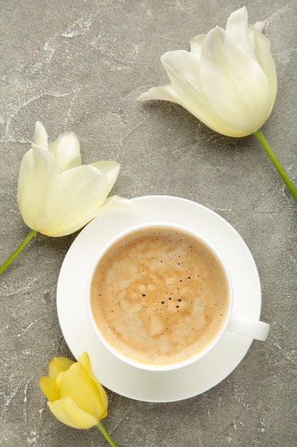 Taza de café con tulipanes blancos sobre superficie gris