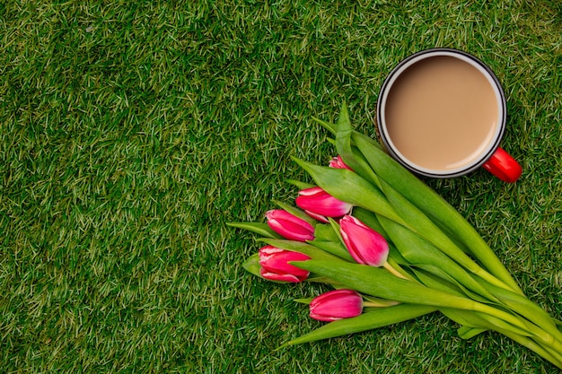 Taza de café y tulipanes sobre hierba verde