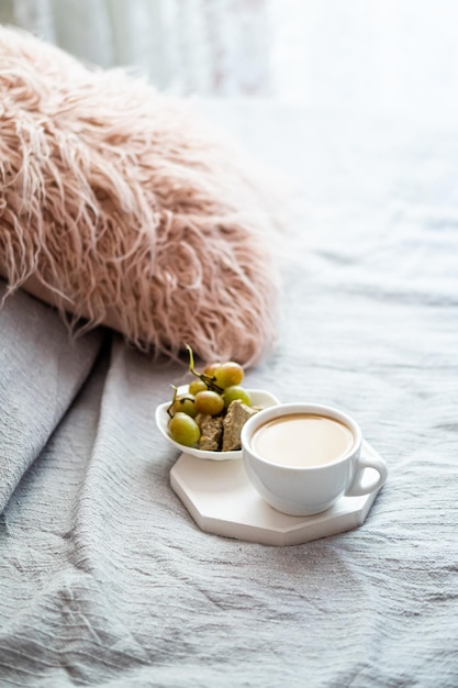 Taza de café y uvas con una acogedora almohada sobre una manta en el interior del dormitorio