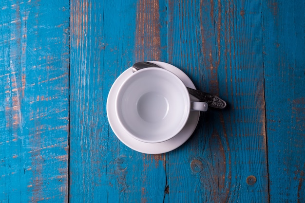 Taza de café vacía blanca en el fondo de madera azul.