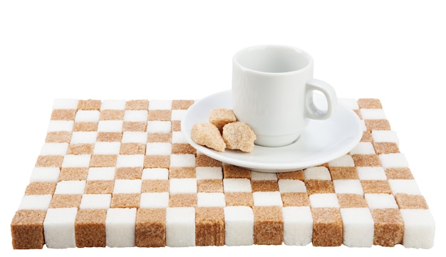 Taza de café vacía en un platillo con tres trozos de azúcar morena sobre un soporte de azúcar blanca y morena.