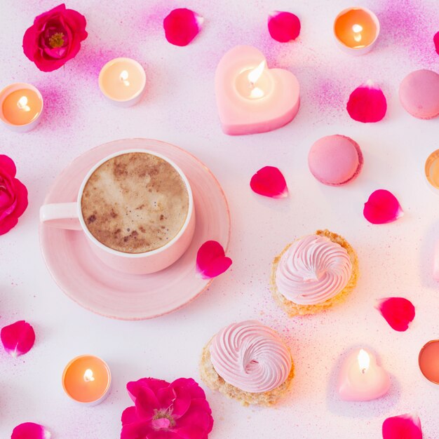 Taza de café con velas encendidas y rosas sobre papel pintado de rosa