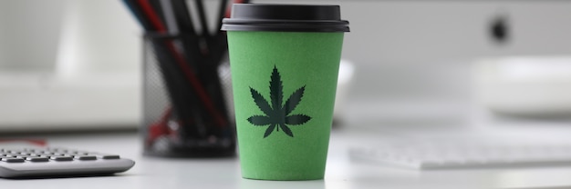 Taza de café verde con logo de cannabis en la oficina tabl