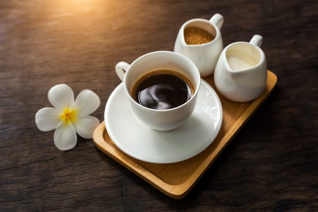 Taza caliente de café negro con decoración de flores blancas en la mesa