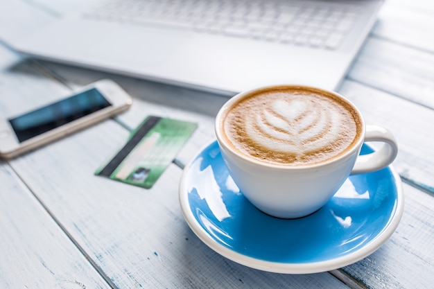 Taza de capuchino art coffee smartphone tarjeta de crédito y portátil blanco.