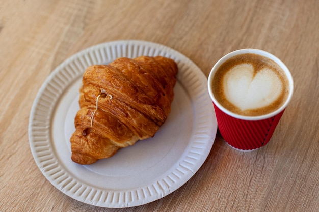 Taza de capuchino con arte latte y croissant en mesa de madera