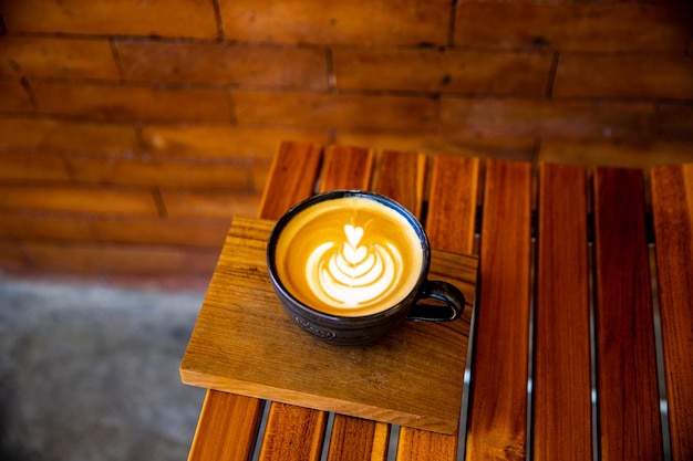 Taza de capuchino con arte latte sobre fondo de madera Hermoso escritorio de madera de espuma y pared de ladrillos