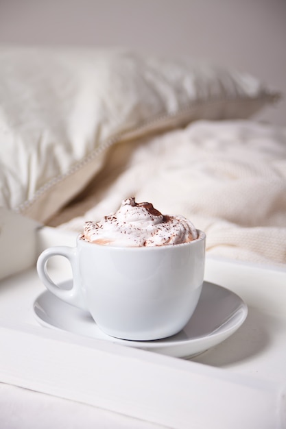 Taza de capuchino en bandeja blanca en la cama temprano en la mañana