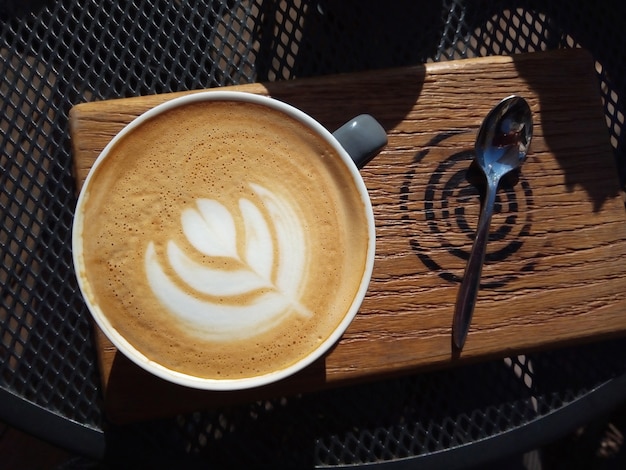 Foto taza de capuchino en el café en un día soleado servido en zanjadora de madera en la mesa de metal de rejilla disfrute de la mañana