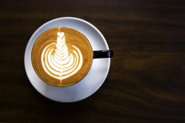 Taza de capuchino caliente está sobre la mesa de madera. Es un arte en el café con leche.