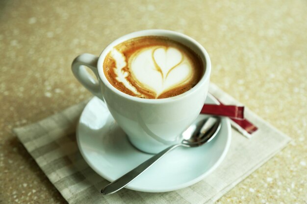 Taza de capuchino con corazón de espuma en la mesa de café