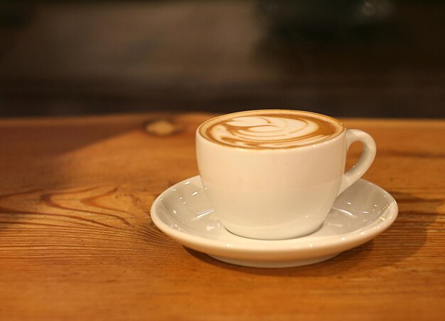 Una taza de capuchino está sobre la mesa junto a la ventana. Es de noche.