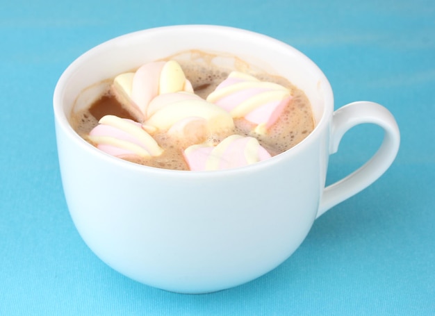 Taza de capuchino con malvaviscos sobre fondo azul.