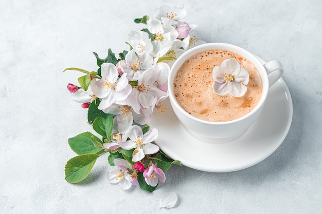 Una taza de capuchino por la mañana y una rama de un árbol en flor sobre una pared gris