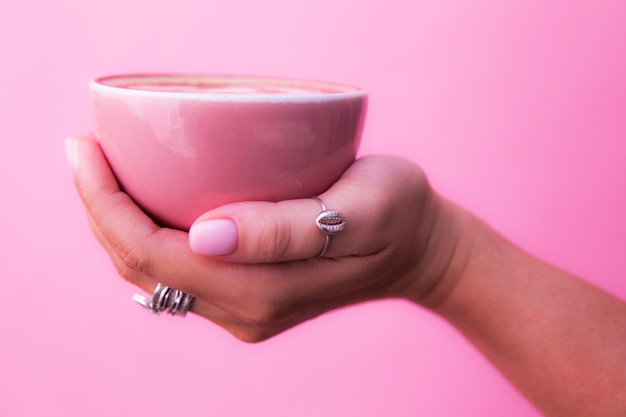 Taza de capuchino de moda rosa sostenida por las manos de una mujer hermosa